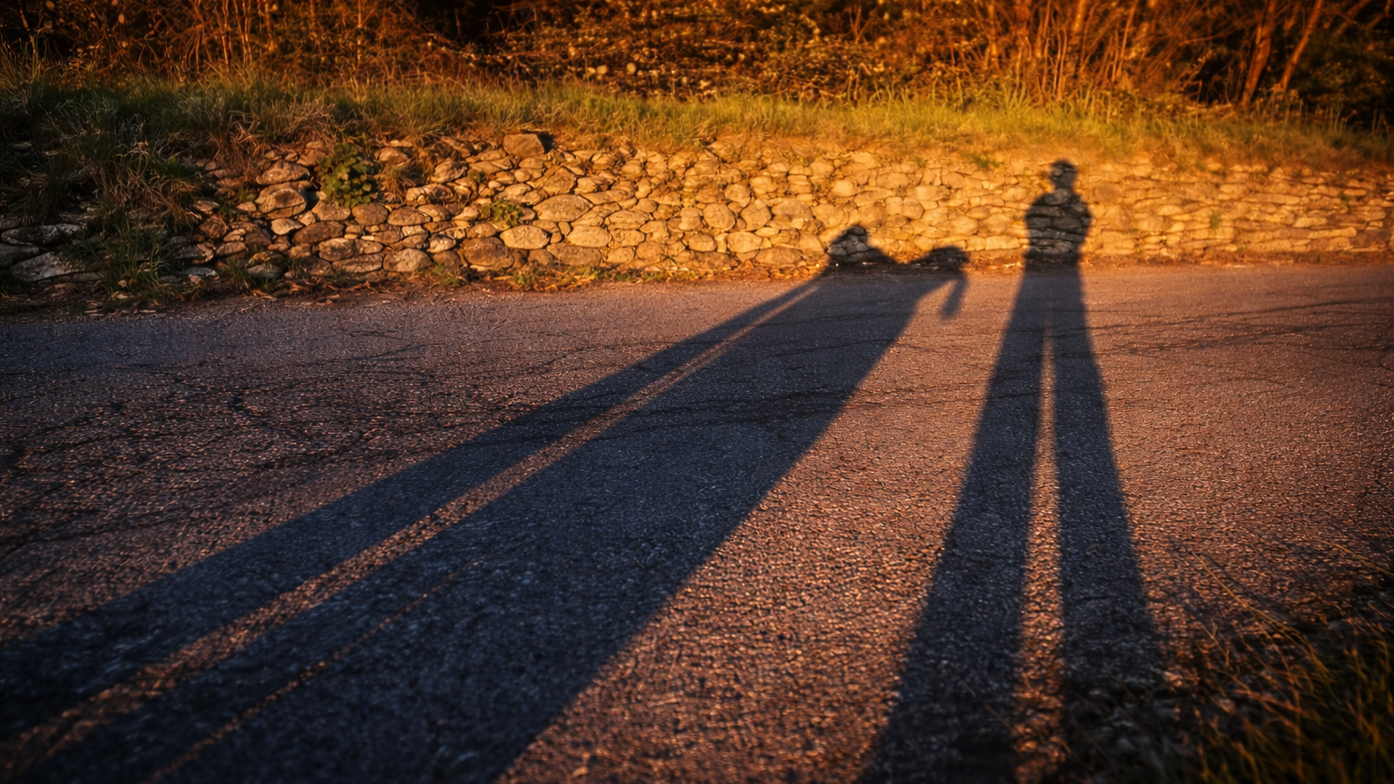 Ombra lunga di moto e pilota su asfalto al tramonto — il dopo che diventa mai