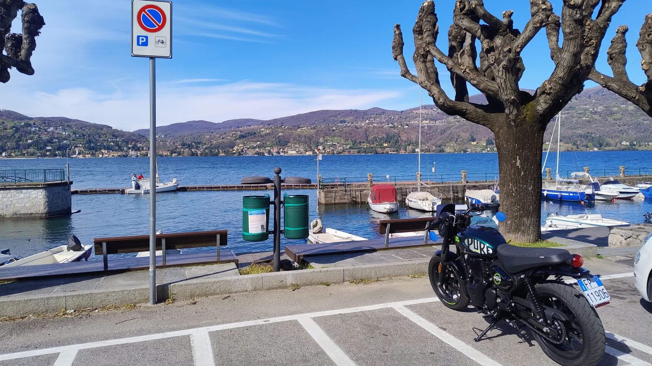 Royal Enfield parcheggiata sul lungolago di Ranco con il porto sul Lago Maggiore